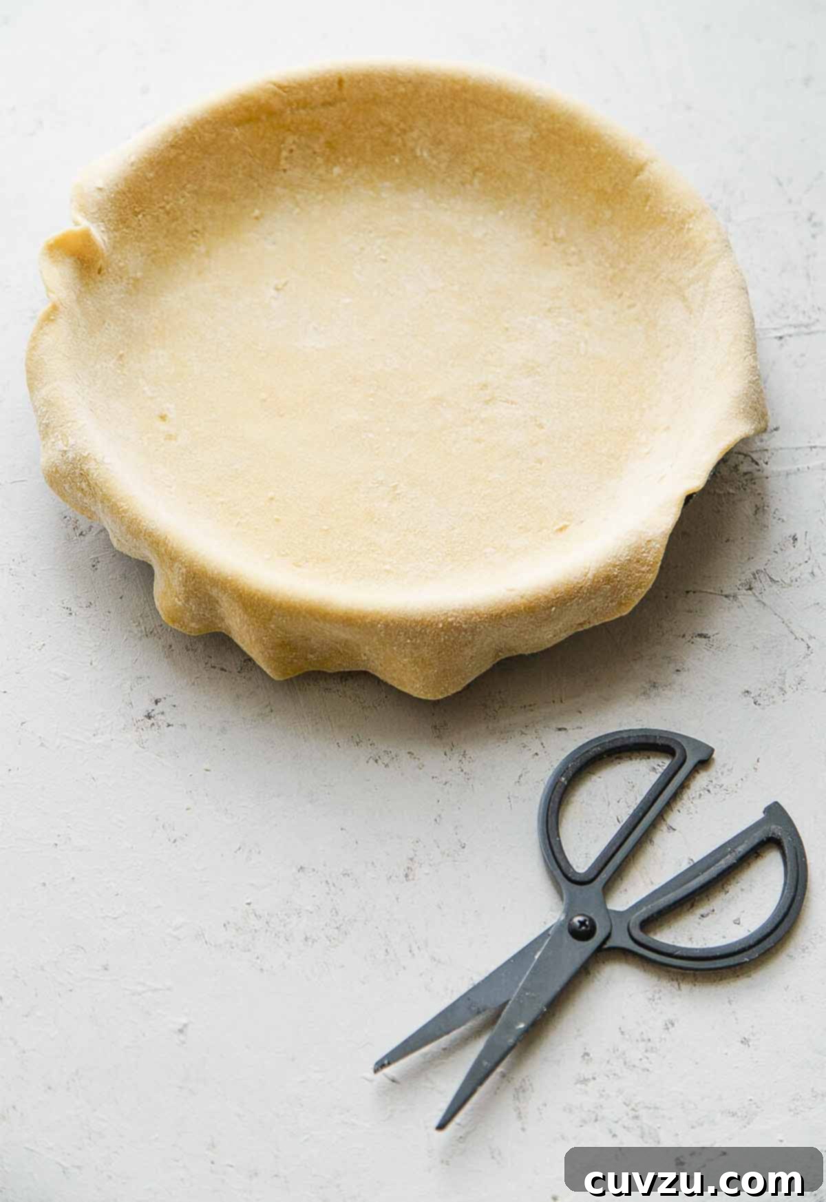 Empty pie crust in a pie plate, with kitchen shears next to it.