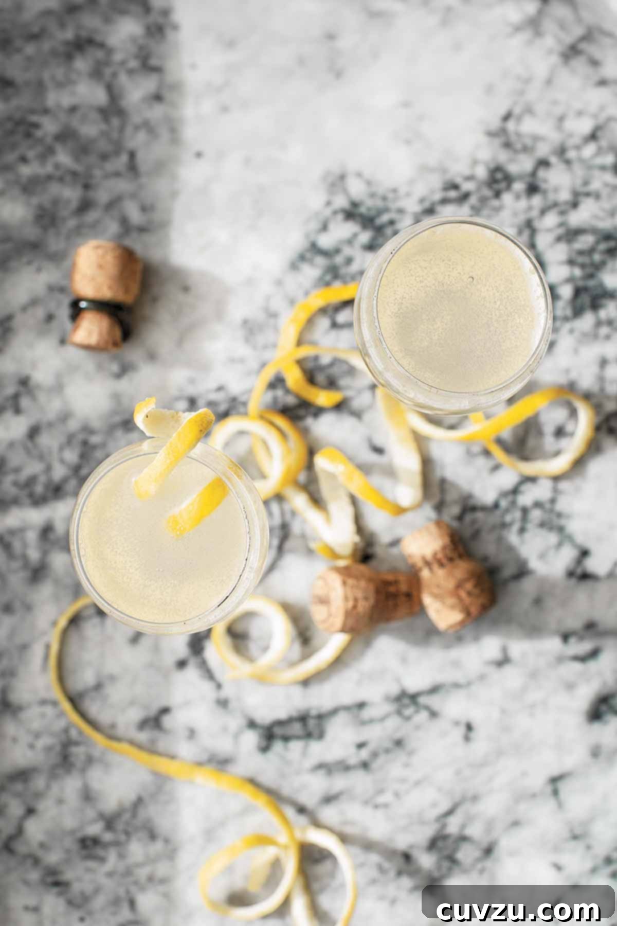 Two flutes filled with homemade sparkling juice topped with lemon twists on a marble surface.