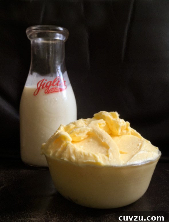 Homemade cultured butter mounded up in a yellow bowl with a glass jar of cream behind it.