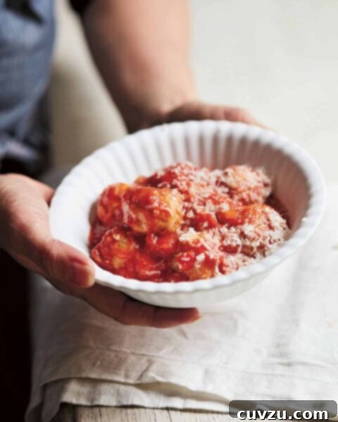 Classic Italian Meatballs 3 Italian style meatballs in a white bowl with grated cheese, being held over a table.