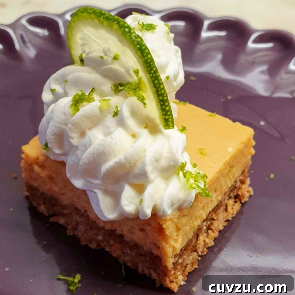 Key Lime Dream Bars 6 A square key lime pie bar with whipped cream and a lime slice on top on a purple plate.