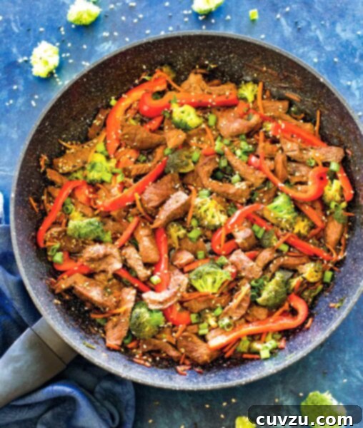 Easy beef stir fry, garnished with scallions and sesame seeds, in a large skillet on a counter.