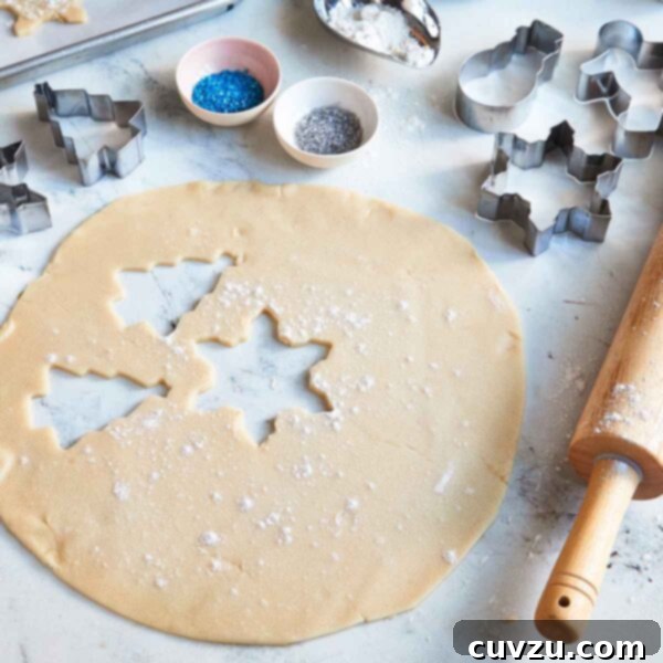Jolly Yuletide Sugar Treats 3 Christmas sugar cookies being rolled out and placed on a sheet pan, with cookie cutters, a rolling pin, sprinkles, and flour nearby.