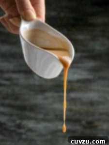 Chicken gravy being poured out of a white gravy boat.