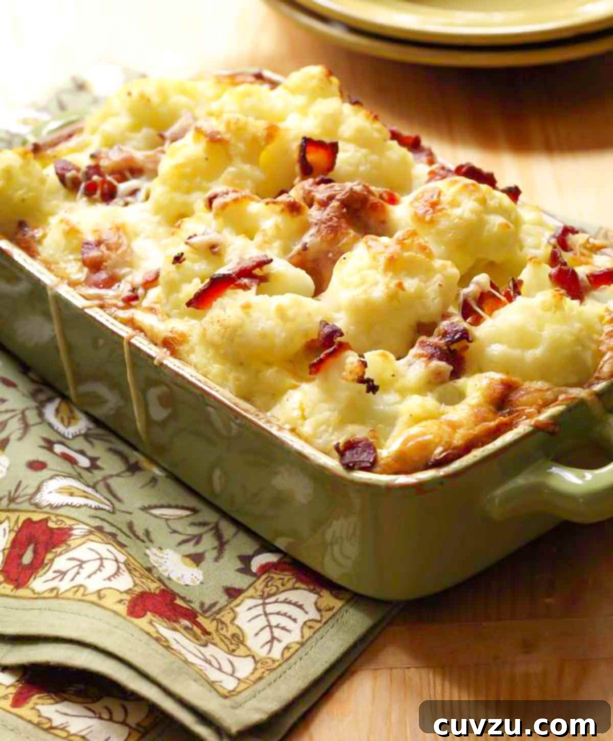 A comforting cauliflower bacon gratin, baked to golden perfection with melted cheese, served in a large, inviting green rectangular baking dish, promising a rich and savory experience.
