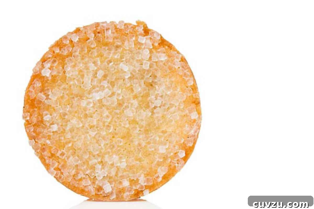 A single, perfectly baked French sable cookie rests on a clean white background, showcasing its delicate, crumbly texture and golden edges, a true representation of refined simplicity.