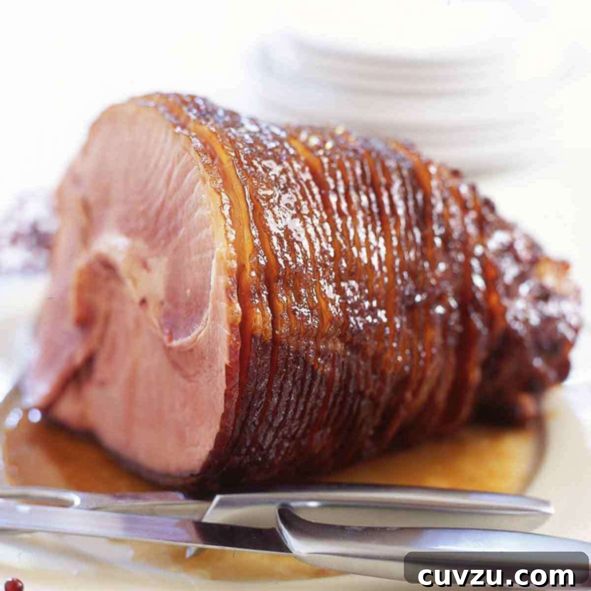 A glazed spiral cut ham on a white platter with a carving knife and fork nearby.