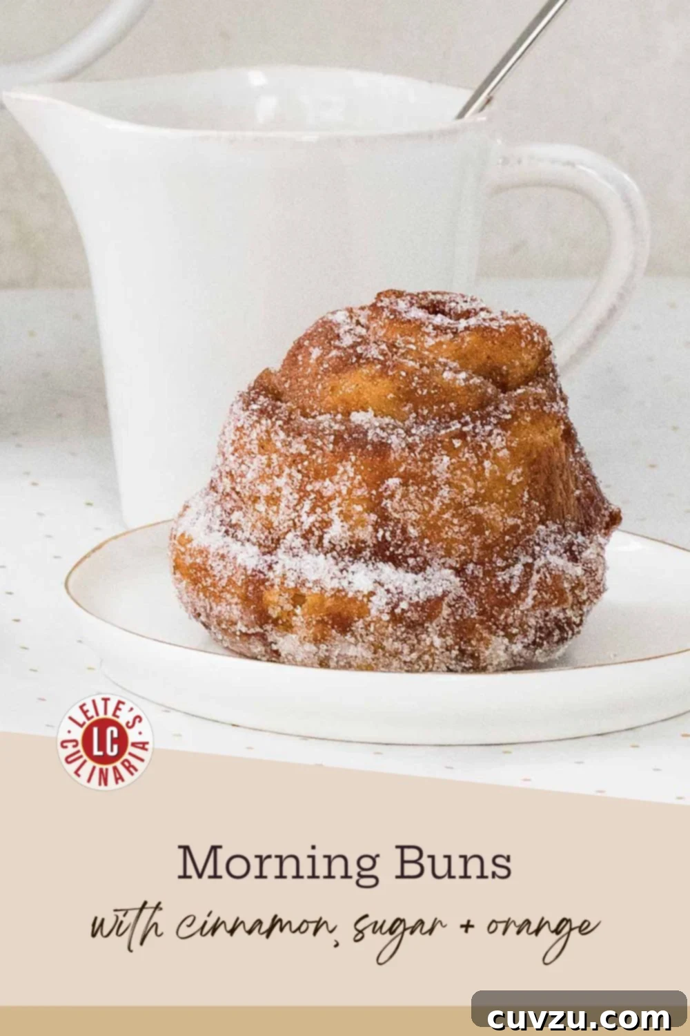 Golden Breakfast Spirals 3 A single fluffy, sugar-coated morning bun with visible flaky layers, resting on a small white plate with a subtle gold rim.