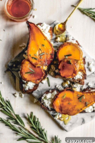 Roasted pear with honey and rosemary on sourdough, on a marble slab tray, beside a jar of honey, a spoon, and sprigs of rosemary.