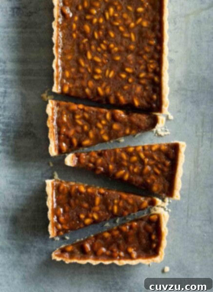 A rectangular pine nut-toffee tart with rosemary and orange cut into triangles, beautifully plated.