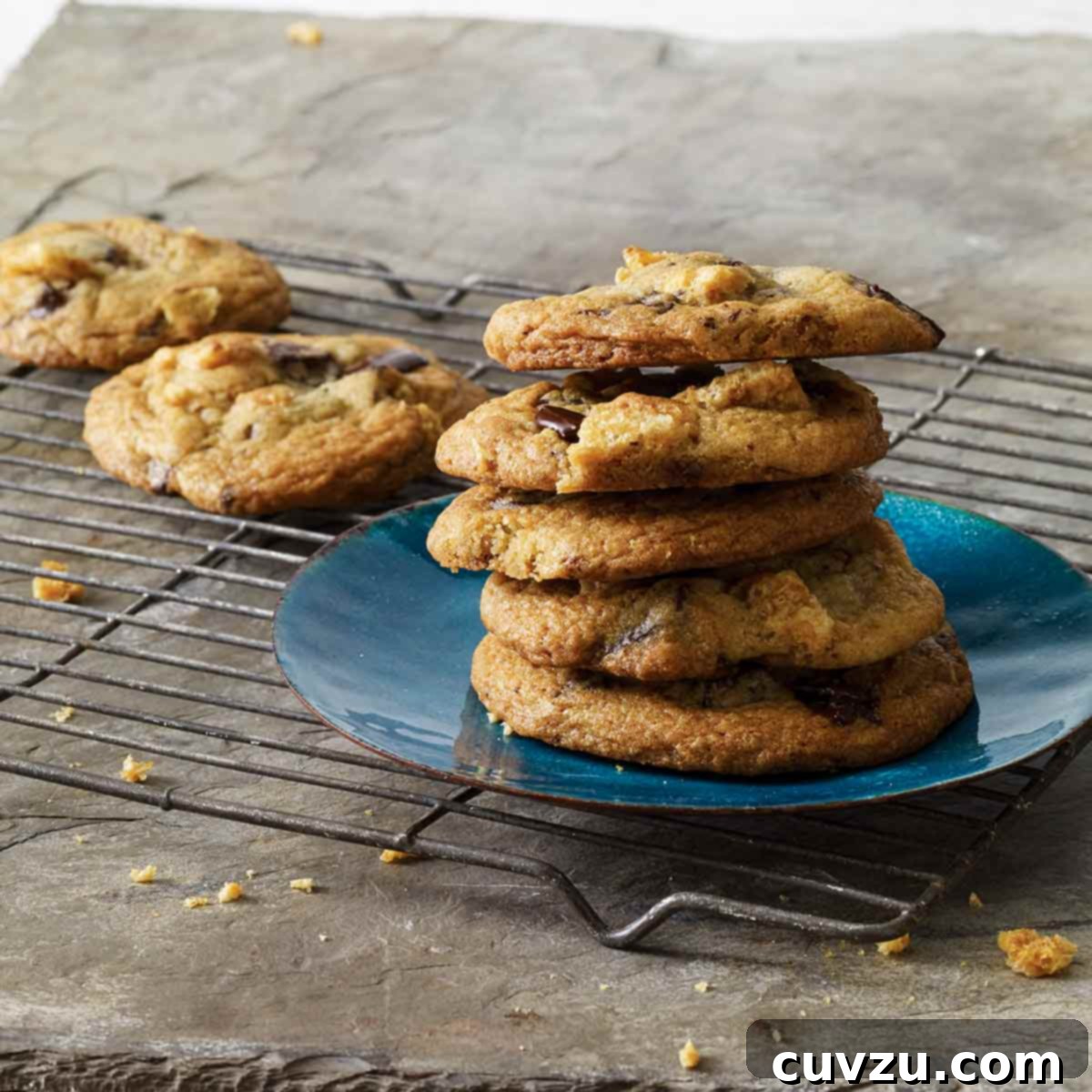 A stack of chicharron chocolate chip cookies on a blue plate on a wire rack with a couple more cookies on the rack.