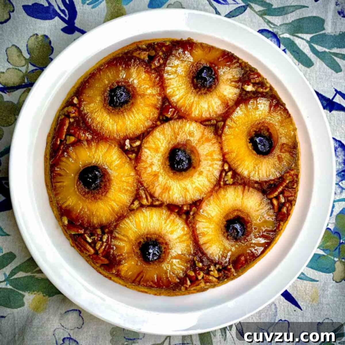 A pineapple upside-down cake on a white plate featuring rich, dark Amarena cherries instead of traditional maraschino cherries.
