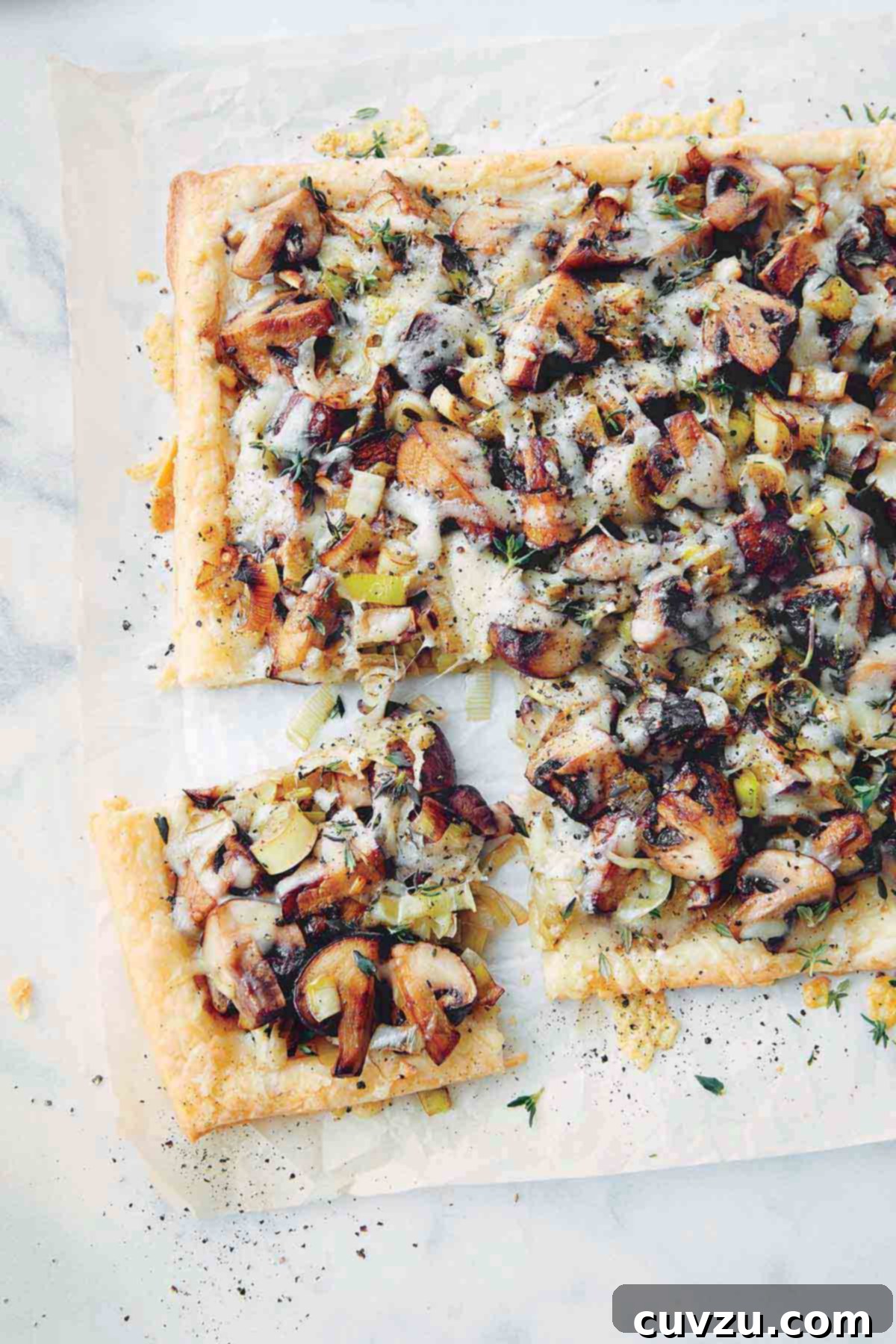 A sheet of parchment paper with a rectangular mushroom, leek, and Gruyere tart, garnished with thyme.