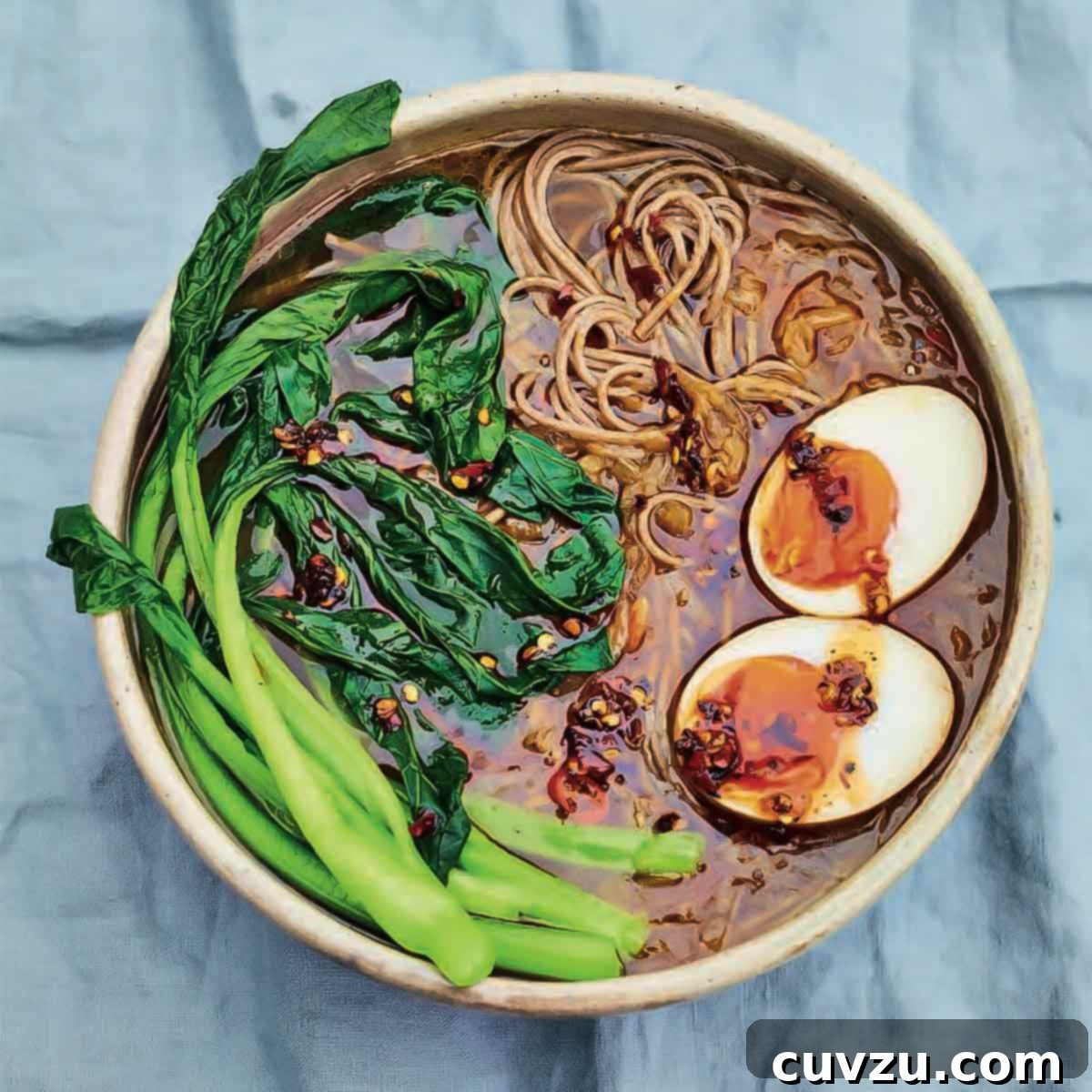 A bowl of caramelized onion ramen with chile, choy sum, and soft boiled egg, showcasing vibrant colors and textures.