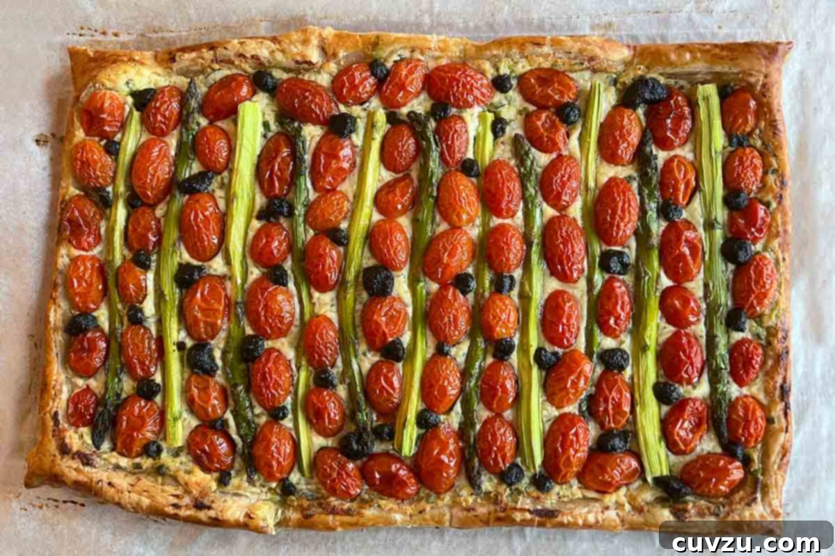 A cherry tomato, asparagus, and herbed ricotta tart on parchment on a baking sheet