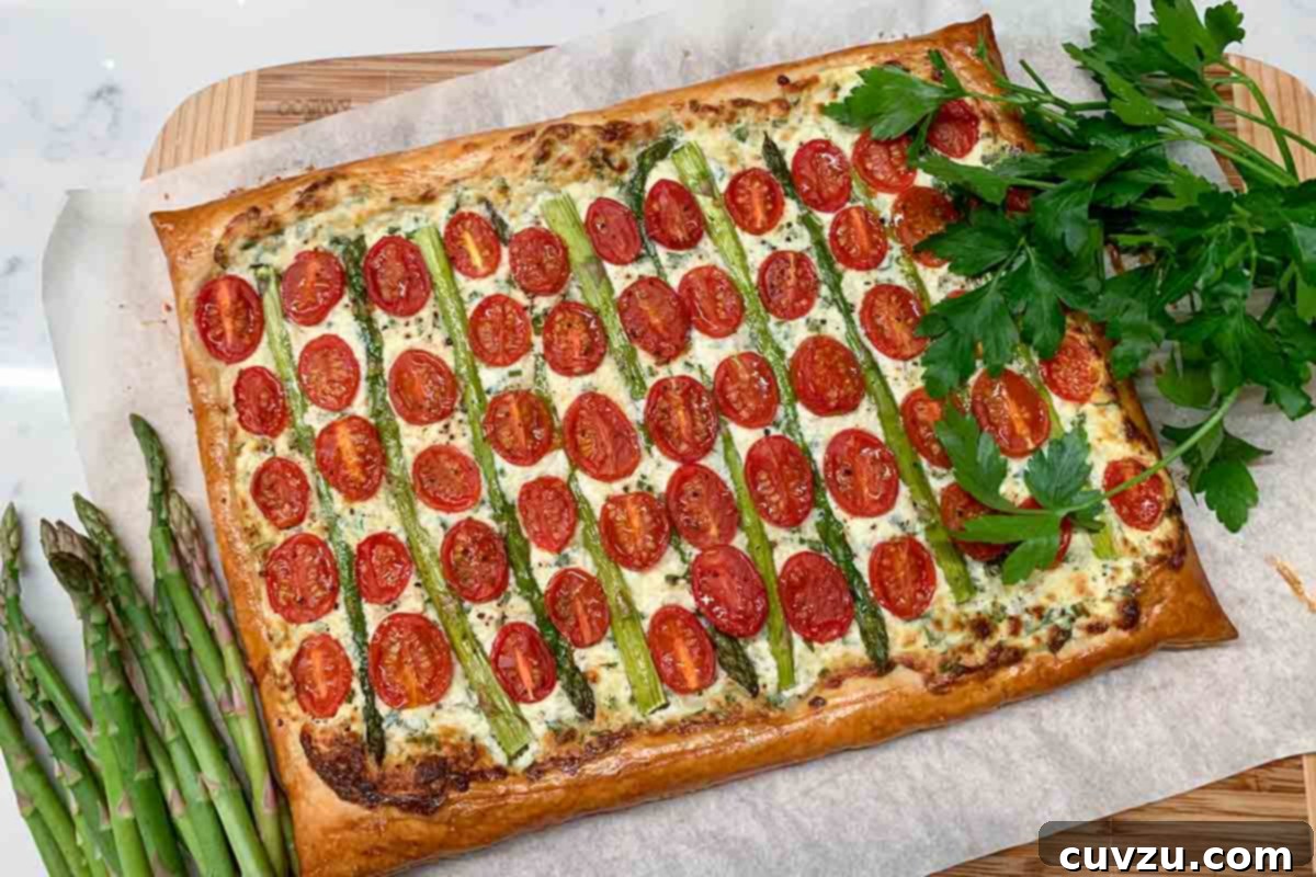 A cherry tomato, asparagus, and herbed ricotta tart on parchment on a baking sheet