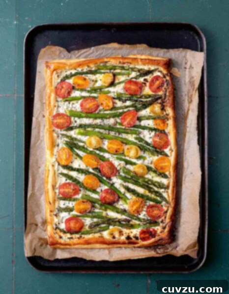 A cherry tomato, asparagus, and herbed ricotta tart on parchment on a baking sheet