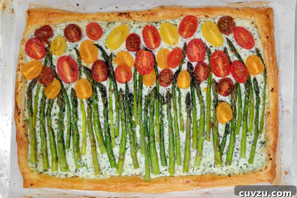 A cherry tomato, asparagus, and herbed ricotta tart on parchment on a baking sheet