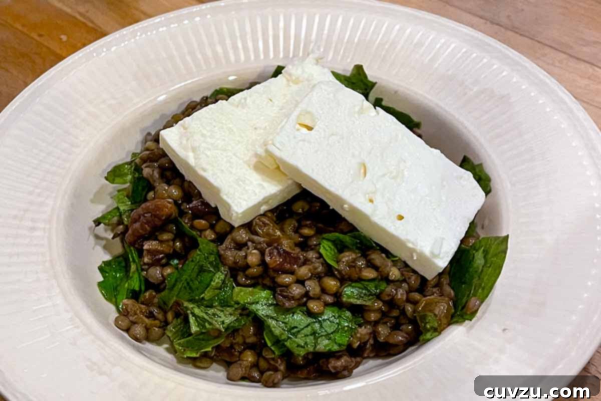 Zesty Marinated Lentil Salad 5 A white bowl filled with warm marinated lentil salad with feta cheese slabs on top.