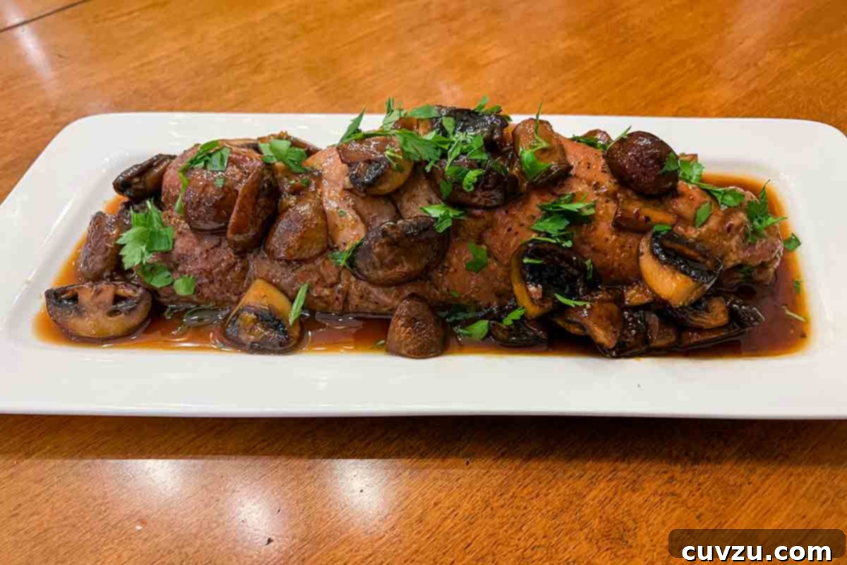 Apricot-Glazed Pork with Earthy Chanterelles 5 A perfectly cooked piece of pork tenderloin, glistening with mushroom and apricot sauce, served on a rectangular platter.