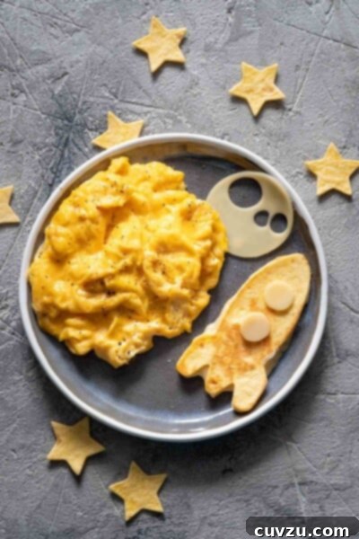 A round plate filled with easy scrambled eggs and a pancake in the shape of a rocket with pastry stars scattered around it