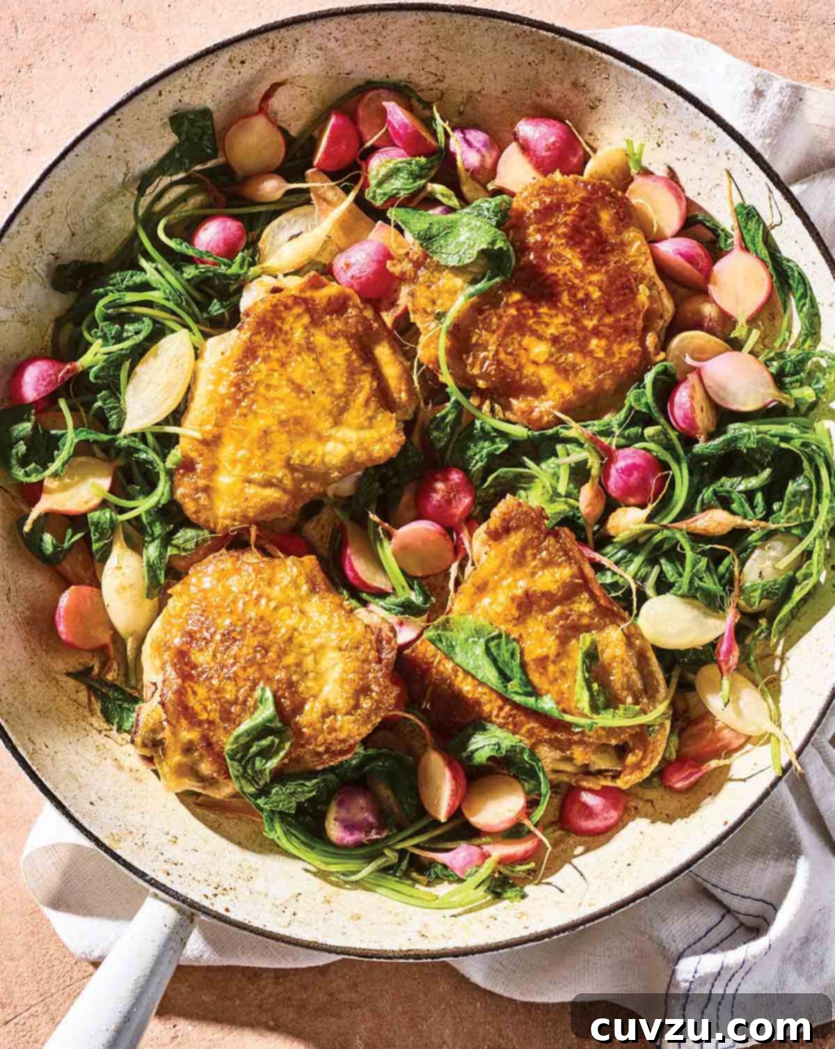 A white enameled skillet filled with golden-brown chicken thighs, halved radishes, and fresh radish greens, ready to serve.