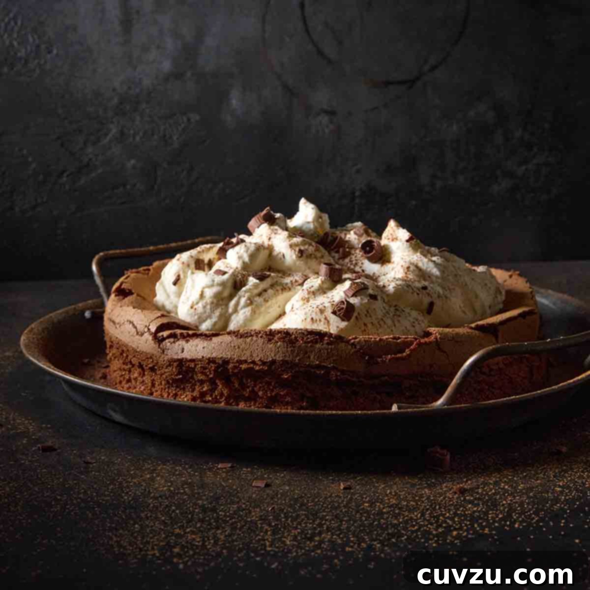 A magnificent flourless chocolate cloud cake, generously topped with billows of fresh whipped cream, on a shining metal platter.