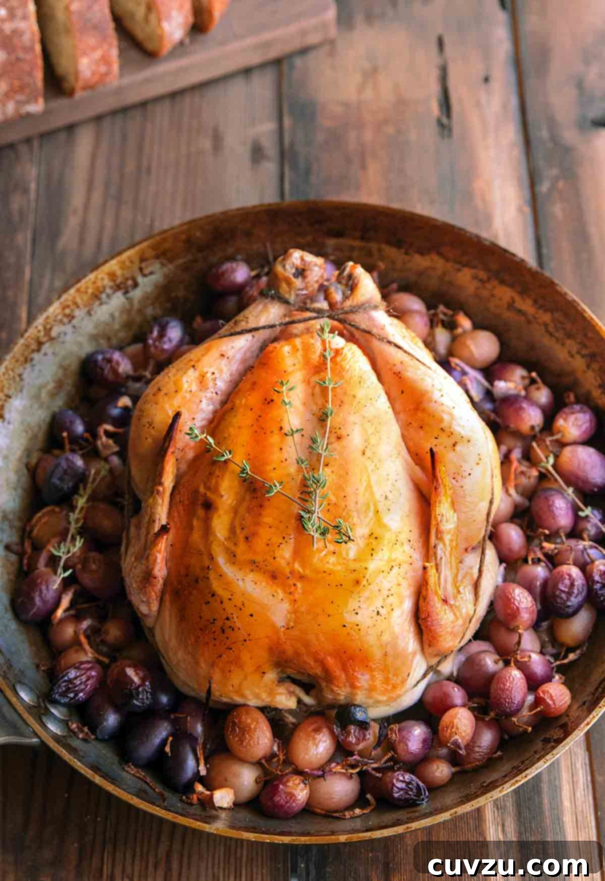 A whole simple roast chicken in a skillet, surrounded by grapes, indicating a delicious and easy meal.