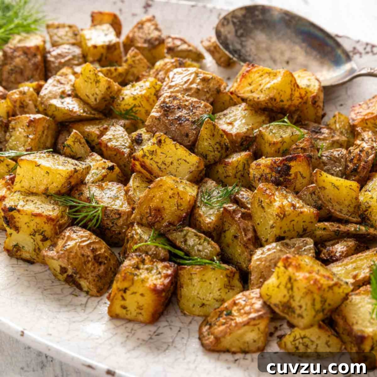 An oval platter generously filled with perfectly cubed roasted potatoes, elegantly garnished with fresh dill.