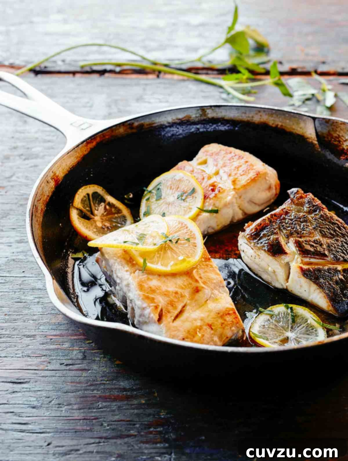 A sizzling skillet featuring three perfectly pan-fried fish fillets, adorned with bright lemon slices.
