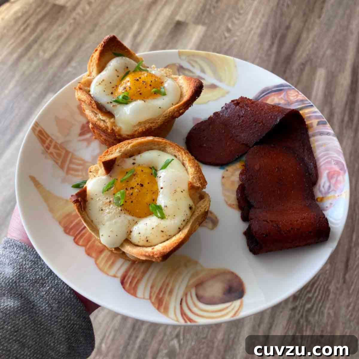 Golden Toast Egg Nests 5 Two baked egg and toast cups on a plate with a strip of bacon