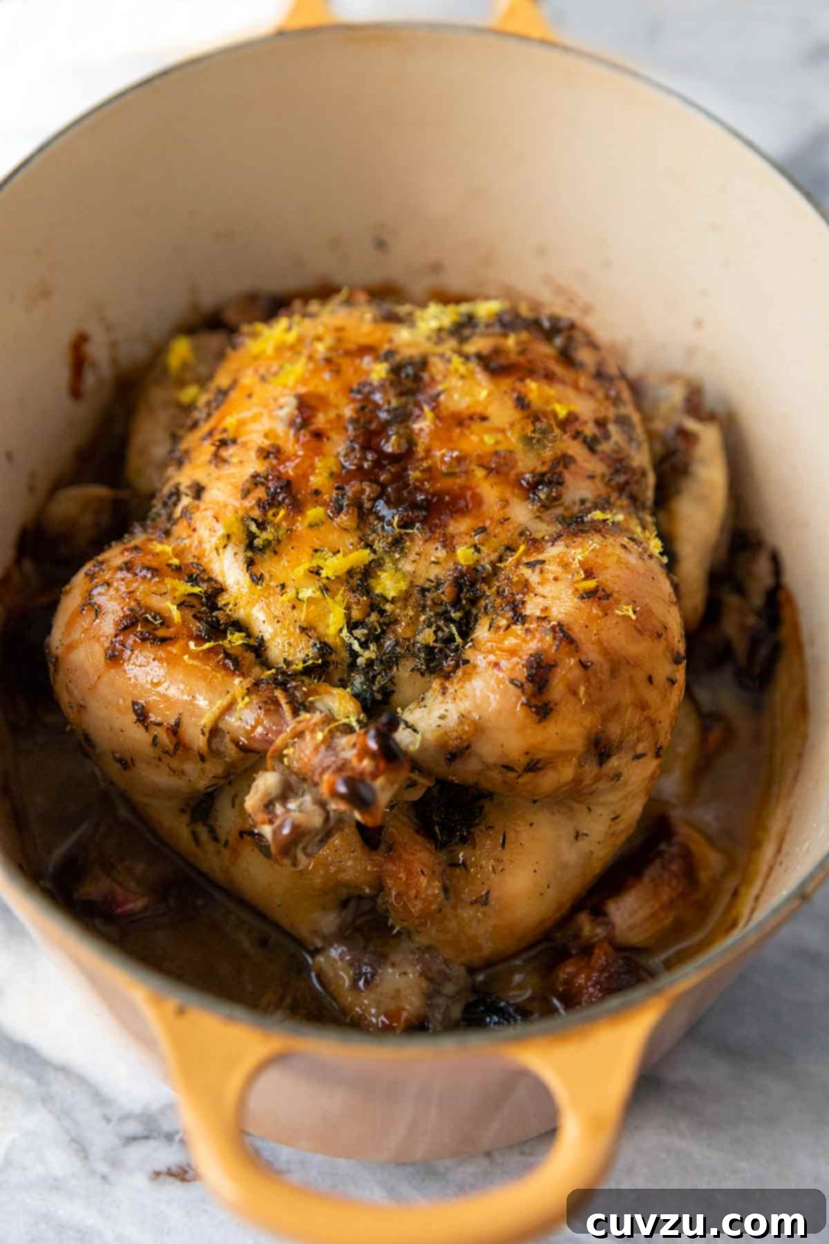 Dutch Oven Roasted Chicken and Caramelized Shallots 10 A large yellow Dutch oven with a roast chicken on a bed of cooked shallots, topped with lemon zest and herbs.