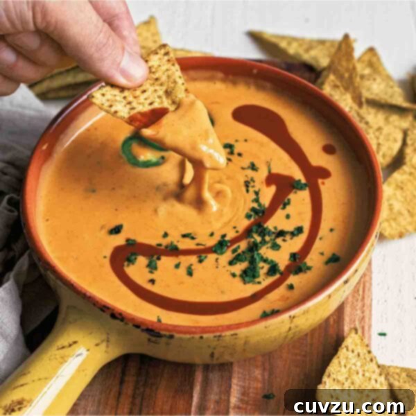 A bowl of easy queso dip, rich and creamy, with a tortilla chip being dipped into it, garnished with fresh cilantro and jalapeño slices.