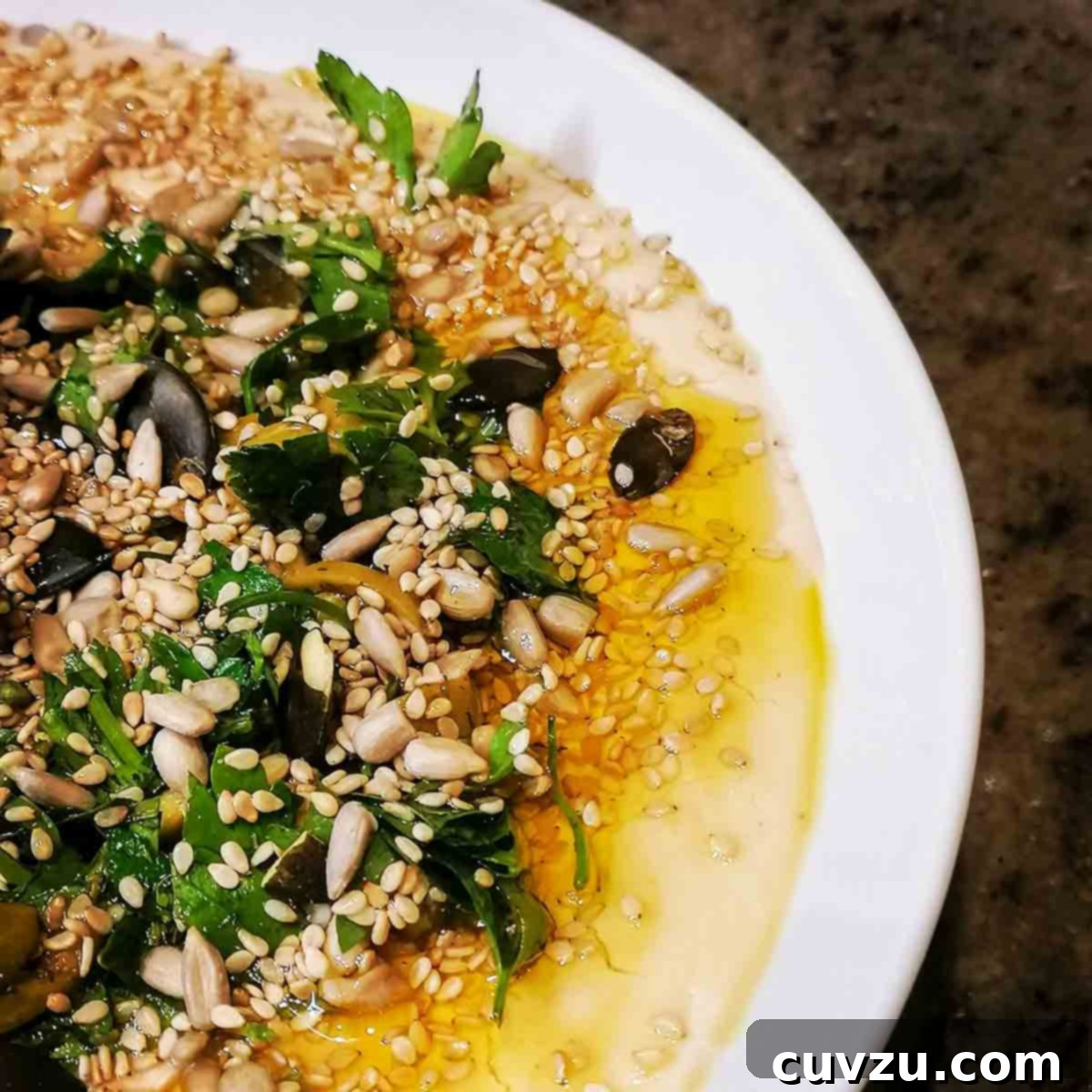 Creamy White Bean Dip 5 A white bowl of white bean hummus topped with seeds, parsley, olives, and oil
