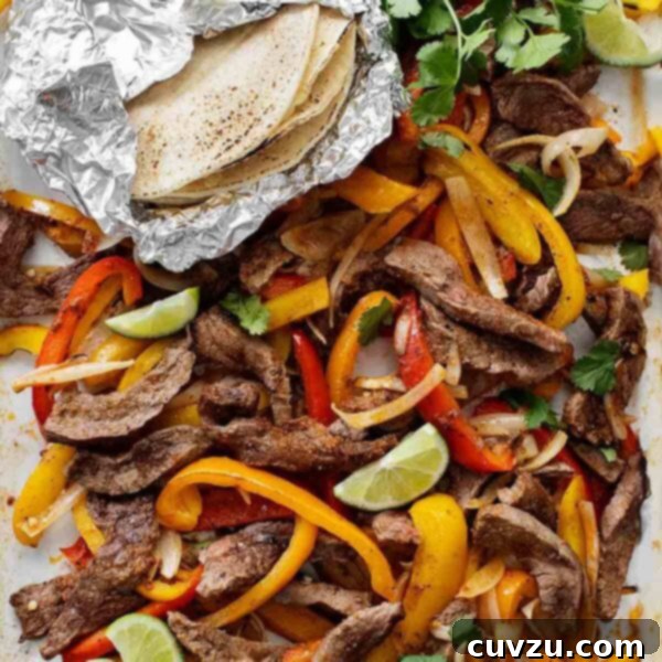 An enamel baking tray filled with sliced peppers, steak strips, onions, lime wedges, cilantro, and a foil packet of tortillas on the side.