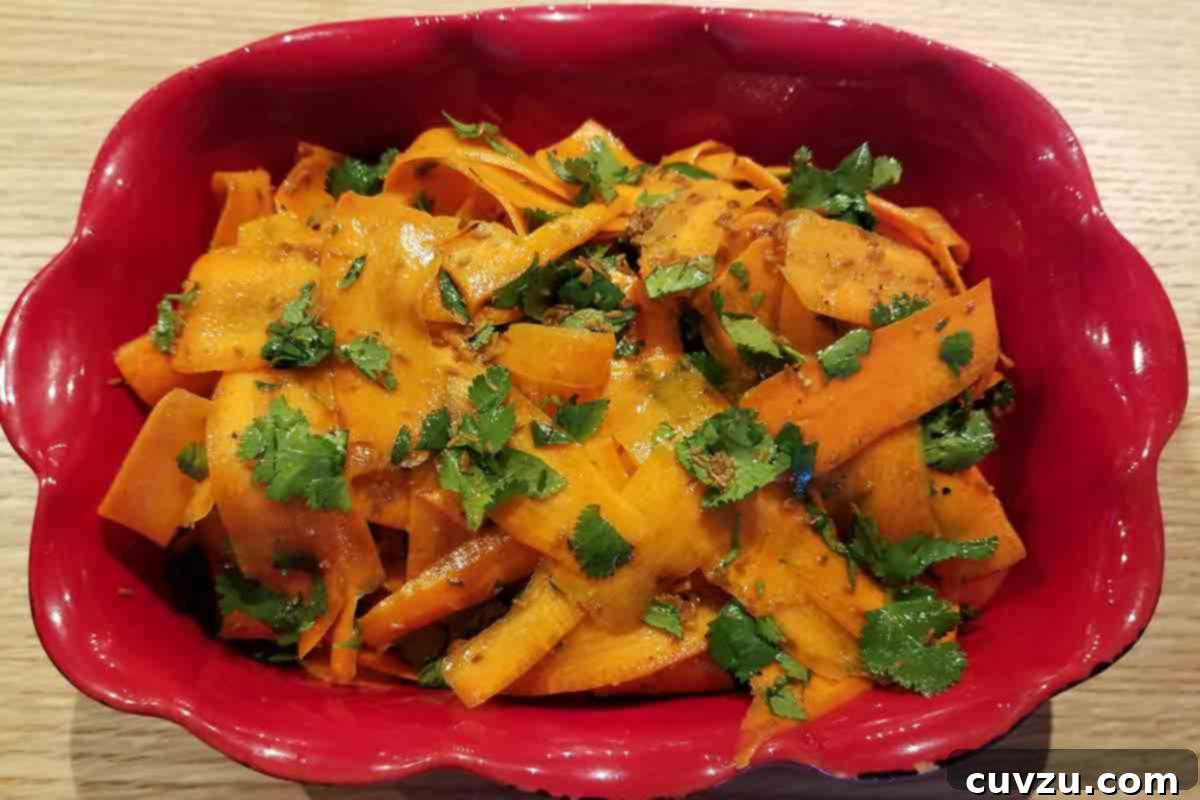 Vibrant Shaved Carrot Salad 6 A vibrant red scalloped serving dish filled with carrot ribbon salad, garnished with fresh cilantro, ready to be served.