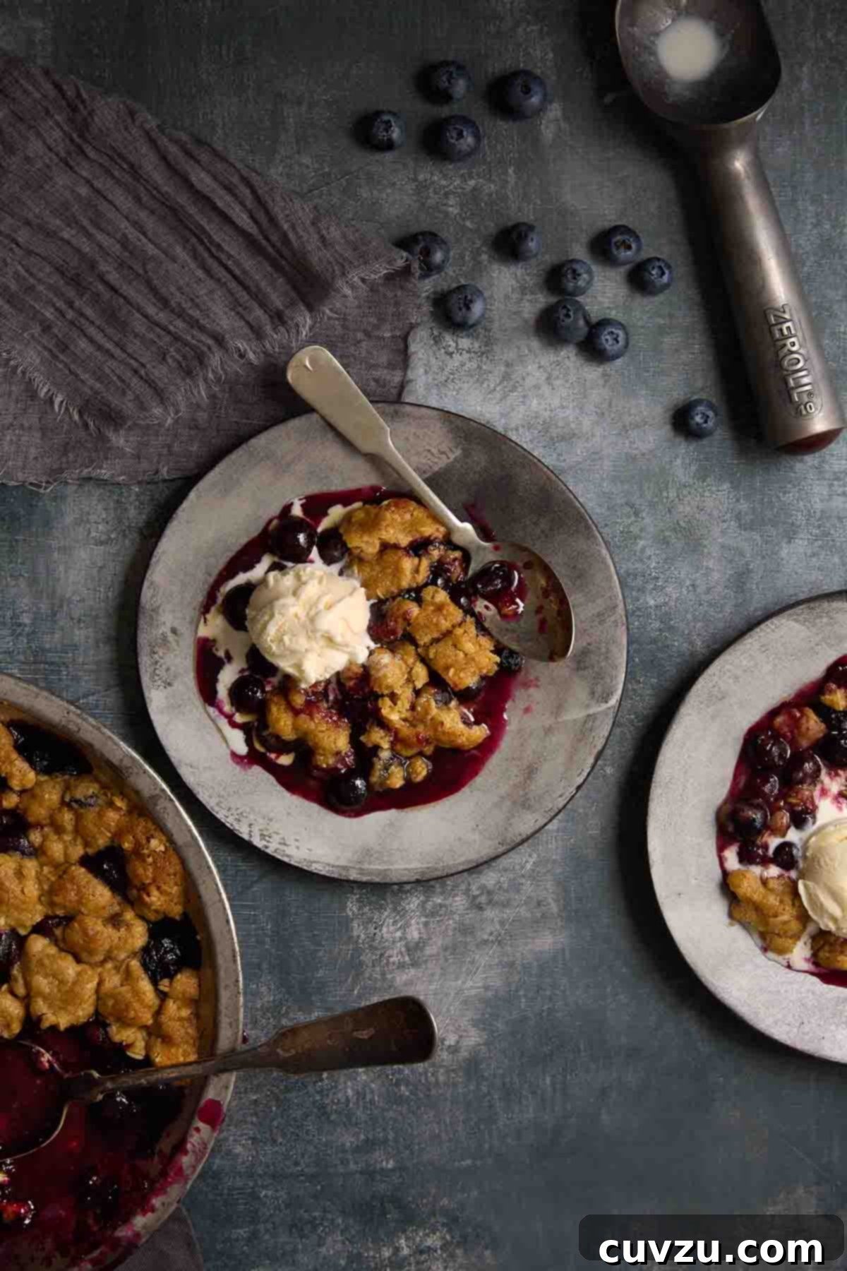 Zesty Lemon Blueberry Scones 3 Blueberry crumble with melted vanilla ice cream and blueberries on a grey plate.