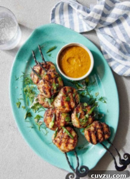 Two grilled scallop kabobs on a blue oval platter with a dish of dipping sauce on the side.