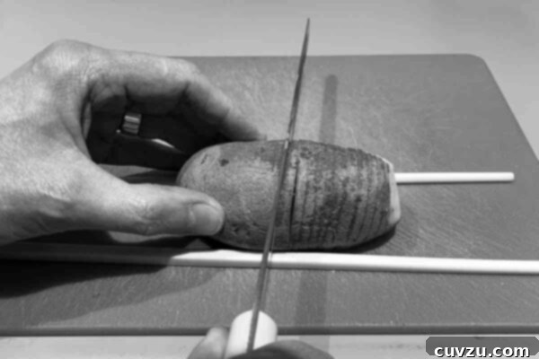 A person using chopsticks as a guide for cutting hasselback potatoes.
