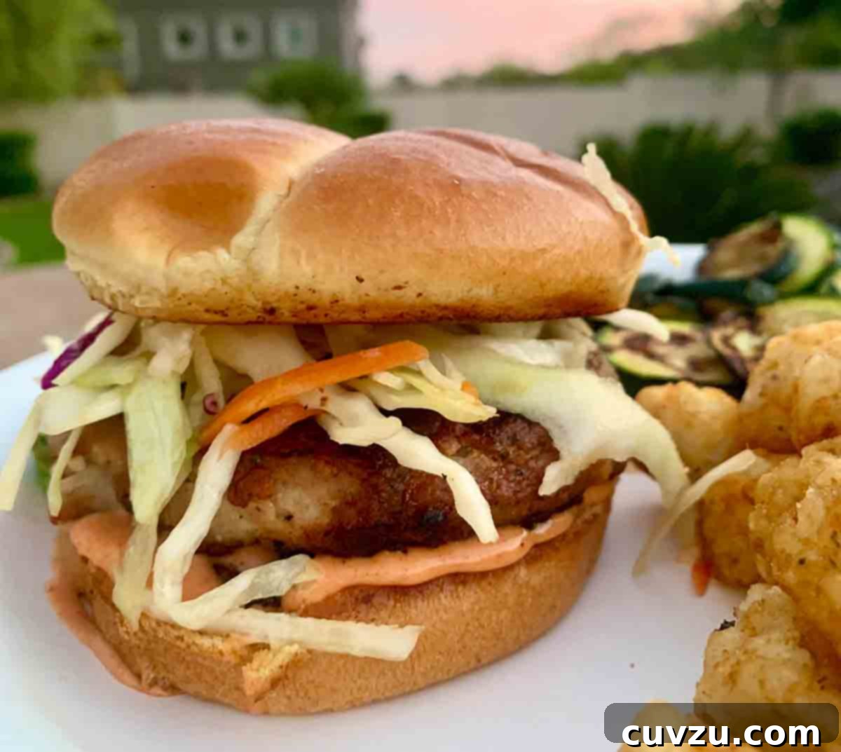 Flame-Kissed Pork Burgers 5 A grilled pork burger topped with coleslaw and tater tots on the side.