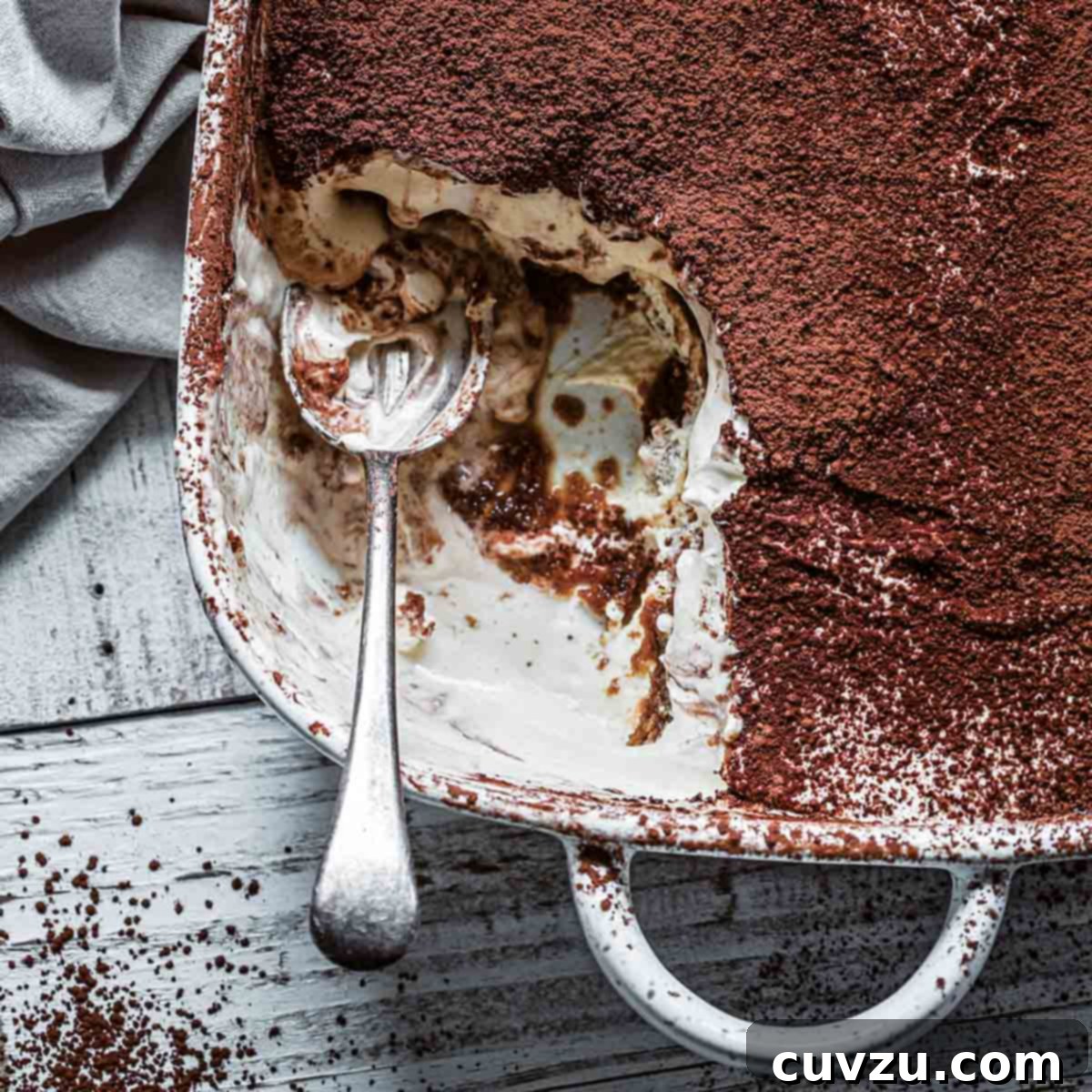 The Quintessential Italian Tiramisu 3 A square baking dish filled with traditional Italian tiramisu with a spoon resting inside and a portion missing.