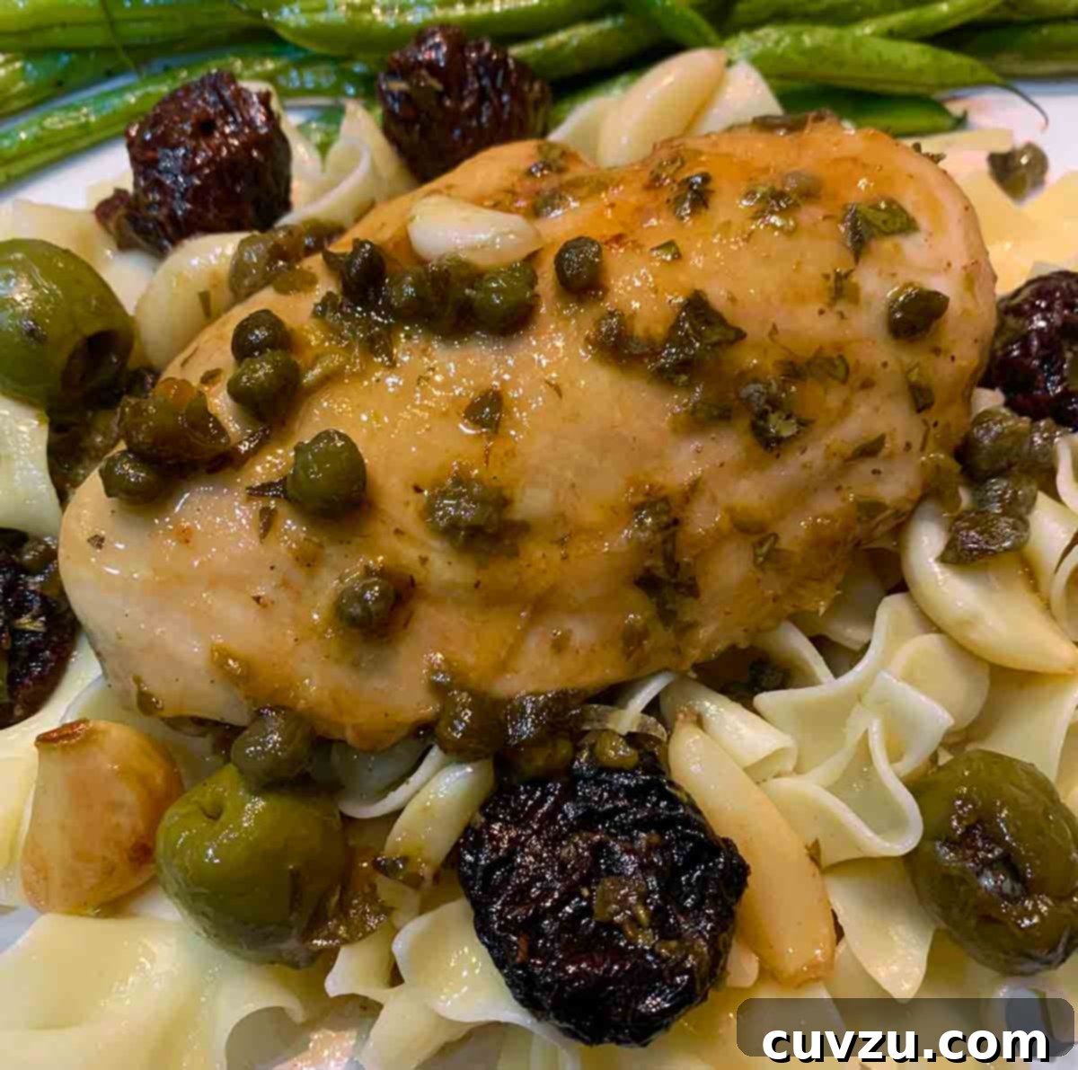 Chicken Marbella Reimagined 5 A pieces of modern chicken Marbella on egg noodles with green beans on the side.