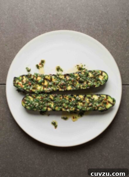 Two grilled zucchini halves on a white plate, topped with mint salsa.