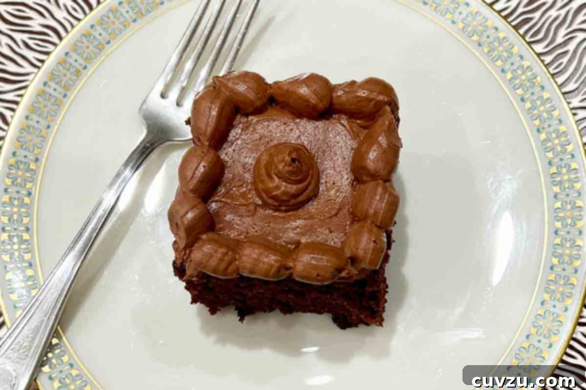 Velvety Chocolate Zucchini Indulgence 5 A square of chocolate zucchini cake with buttercream frosting on a china plate with a fork on the side.