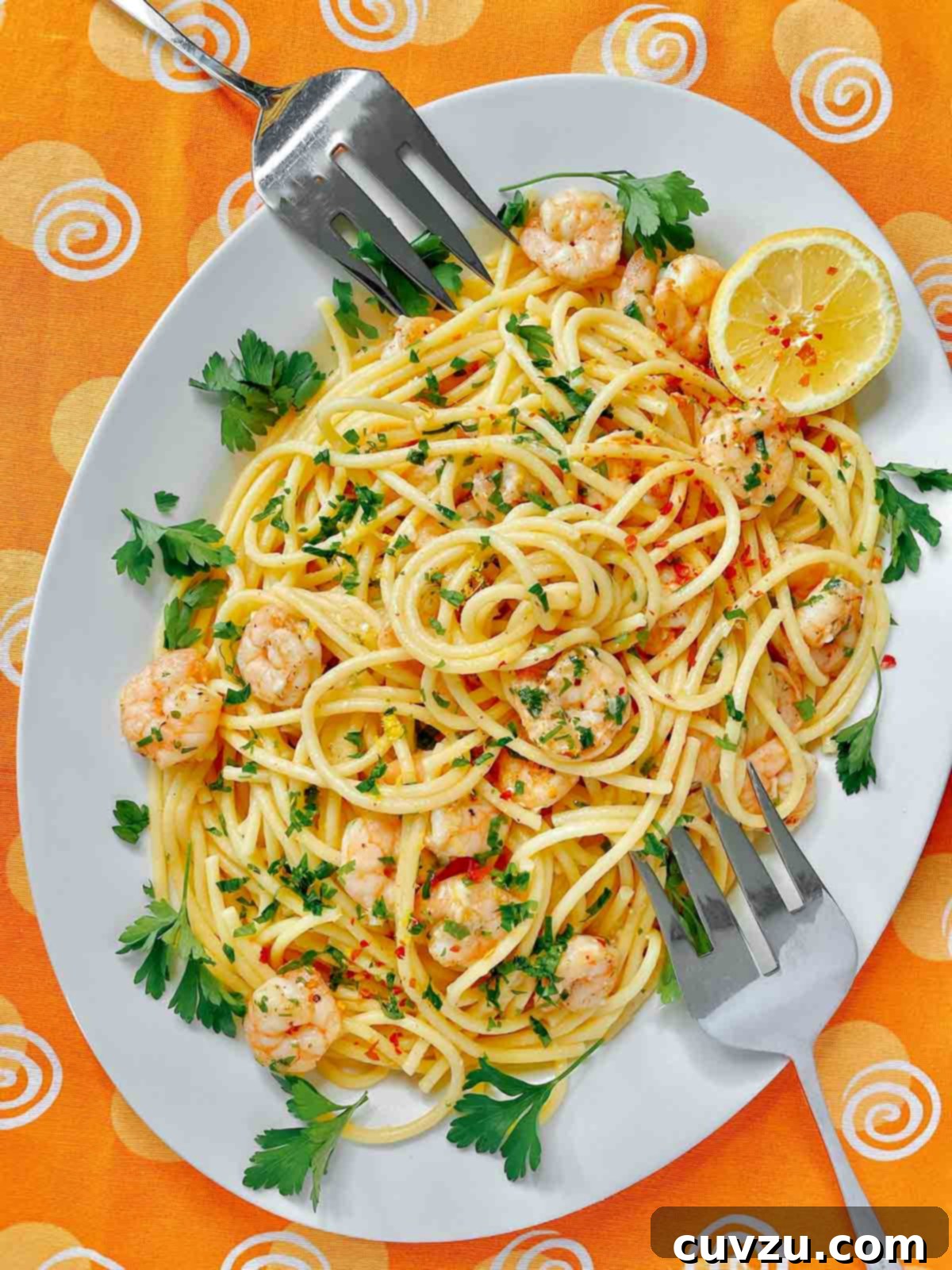 Zesty Lemon Garlic Shrimp Pasta 5 A white platter filled with lemon garlic shrimp pasta, garnished with parsley and a lemon wedge and two serving forks resting on the platter.