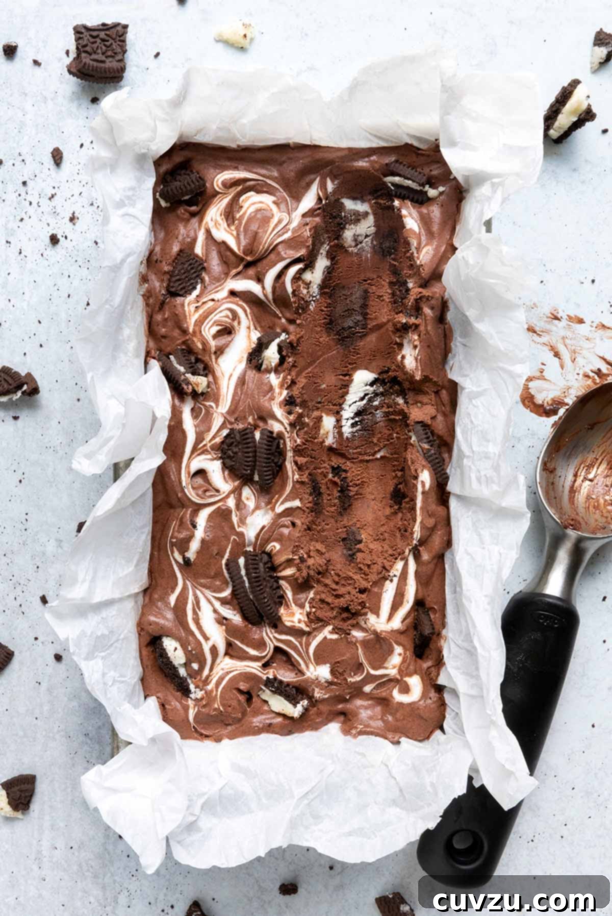 Velvety No-Churn Chocolate Oreo Marshmallow Swirl 3 A loaf pan filled with creamy chocolate Oreo ice cream, adorned with scattered Oreo pieces and an ice cream scoop resting on the side.