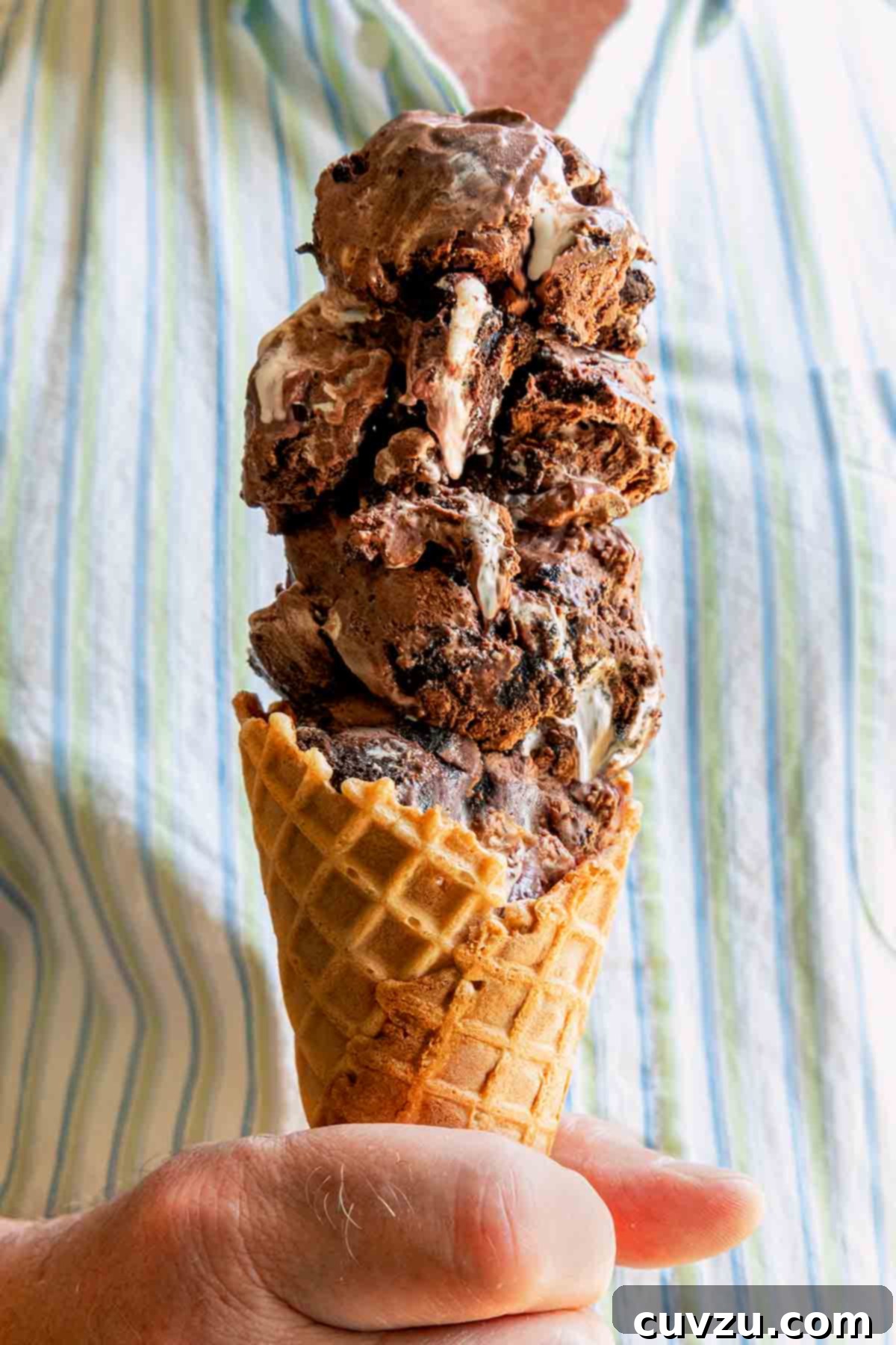 Velvety No-Churn Chocolate Oreo Marshmallow Swirl 4 A man holding a waffle cone generously filled with four scoops of rich chocolate Oreo ice cream, perfect for a summer day.