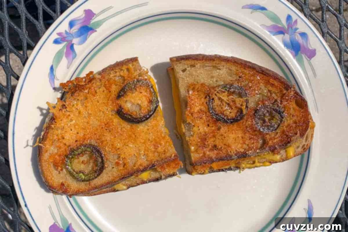 Crispy Parmesan Jalapeño Grilled Cheese 4 A halved Parmesan-crusted grilled cheese with jalapeños on a white decorative plate.