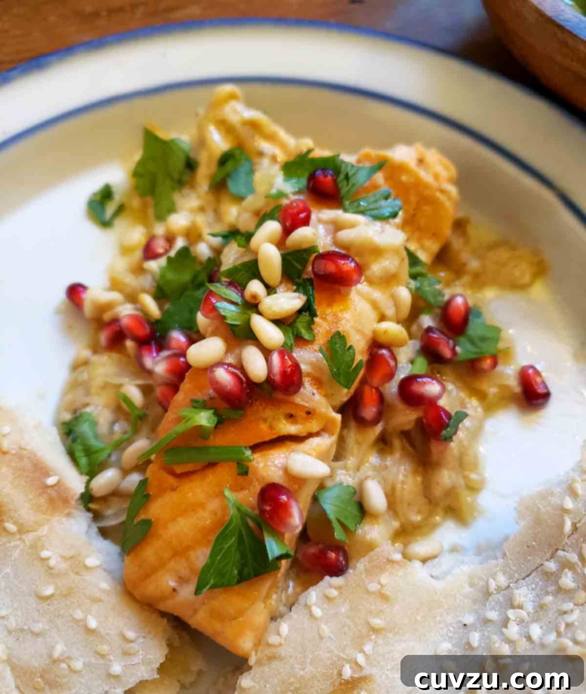 Pan-Seared Salmon with Sweet Tahini Glaze 6 A beautifully plated piece of pan-seared salmon with sweet tahini sauce, artfully garnished with vibrant pine nuts, ruby-red pomegranate seeds, and fresh parsley, presented on a pristine white plate.