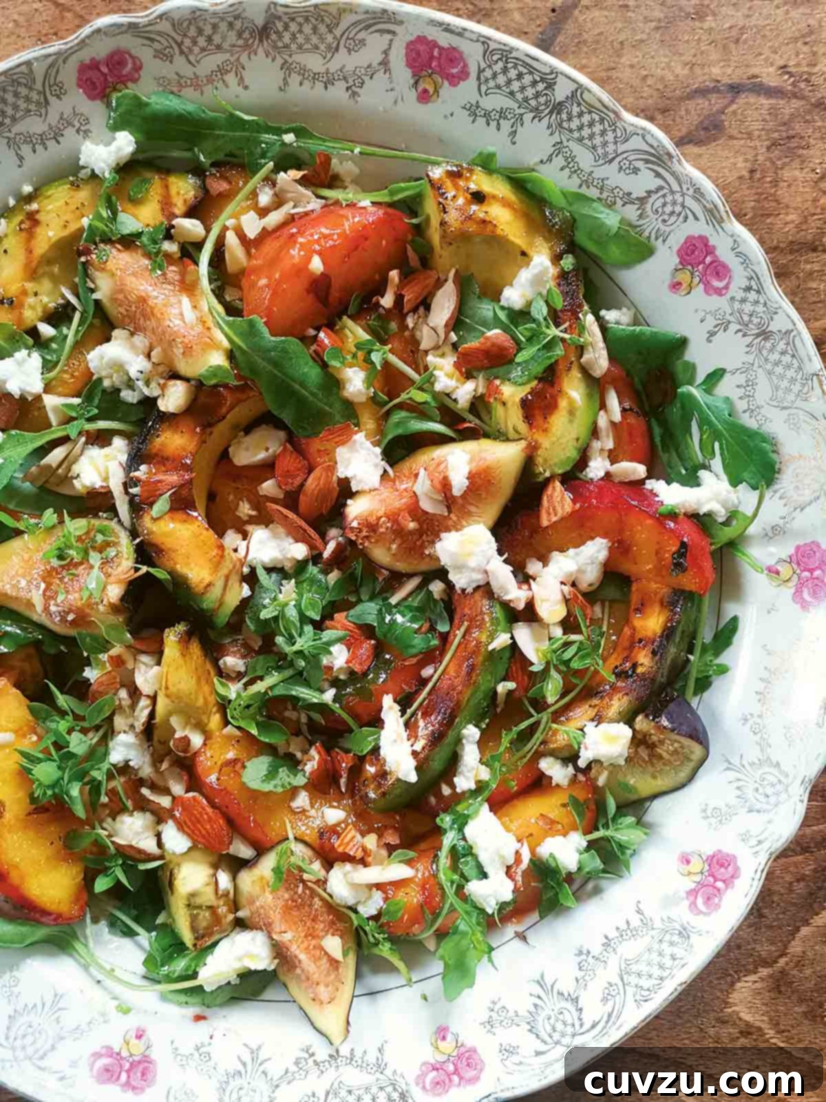 A decorative platter filled with grilled avocado, grilled peach slices, fresh figs, herbs, and goat cheese, highlighting an elegant summer salad.